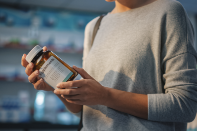 Person holding a dietary supplement bottle while reading the product label inside a retail or laboratory setting.