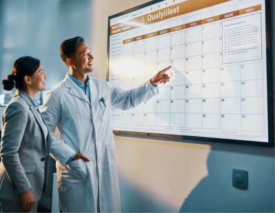 Scientist and quality manager smiling while reviewing a digital calendar display showing organized laboratory analysis schedules.