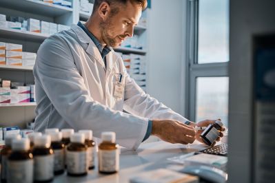 Laboratory professional labeling pharmaceutical bottles on a lab bench with packaged medications.