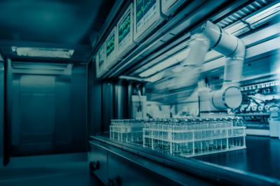 Automated laboratory instrumentation processing rows of sample vials on a stainless steel workstation with digital monitoring screens.